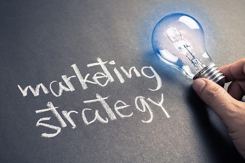 The words marketing strategy with a blue light bulb next to it.