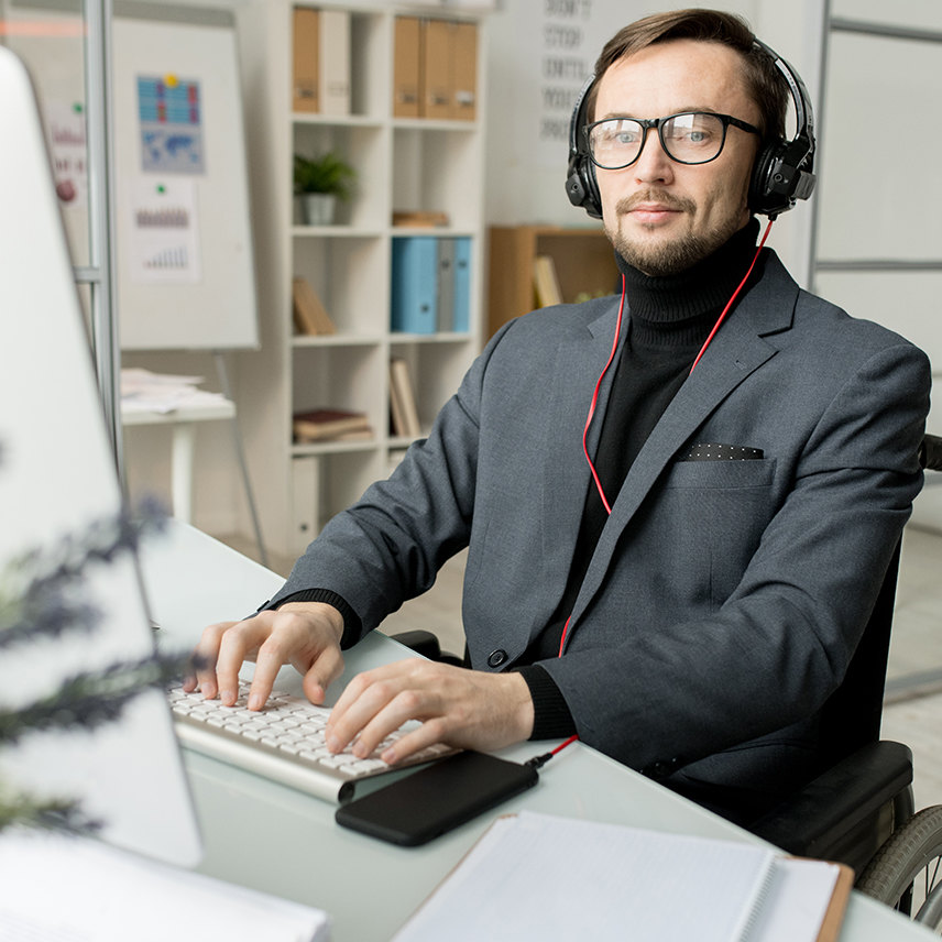 Portrait of business person in eyeglasses and headphones typing on computer at his workplace and listening to music on his mobile phone